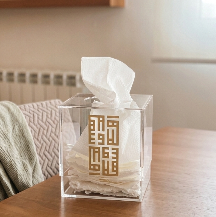 Clear tissue box with gold design on a wooden table in a home setting